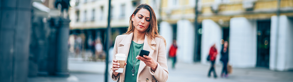 Woman stares at phone concerned with coffee in hand.