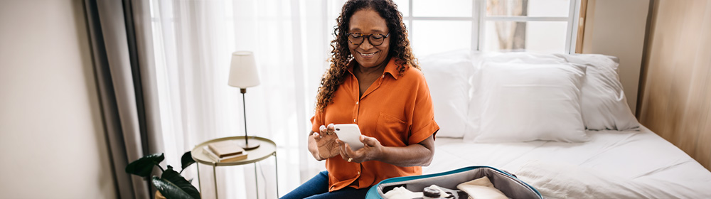 A woman packs for a trip and checks her phone.