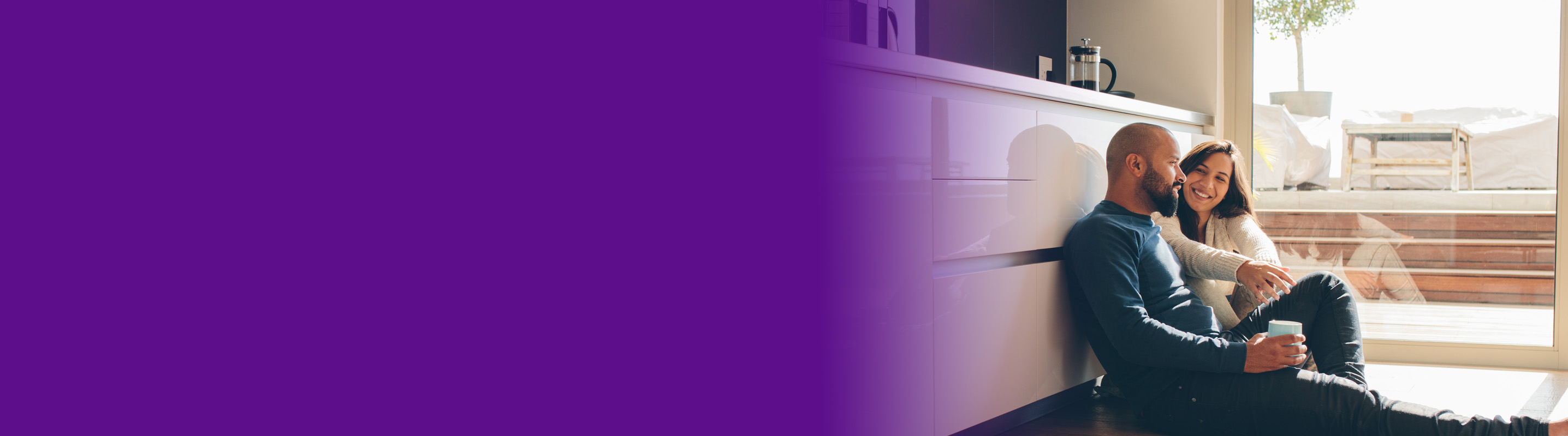 couple smiling on sitting on the kitchen floor drinking coffee